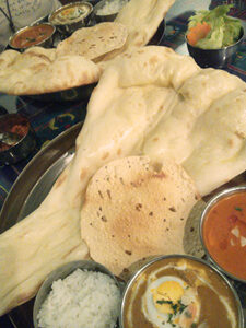 巨大なナンとカレー2種類、ライスとサラダのボウルがテーブルを埋めている。