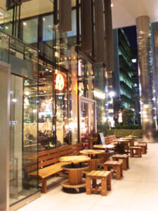 一面ガラス張りの窓の外に並ぶ木製のテーブルとイス。